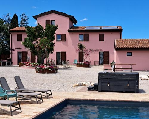 Casa rosa con piscina, lettini e vasca idromassaggio all'aperto.