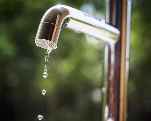 Rubinetto cromato che perde gocce d'acqua con sfondo sfocato.