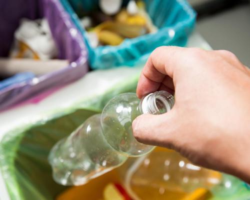 Persona che ricicla una bottiglia di plastica in un bidone differenziato.