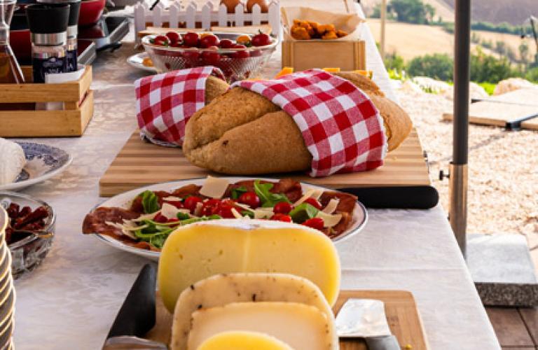 Tavola imbandita con formaggi, pane e vista panoramica sulla campagna.