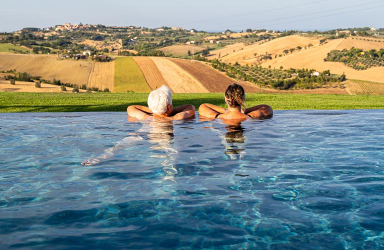 Piscina a sfioro con vista su una villa rosa in campagna.