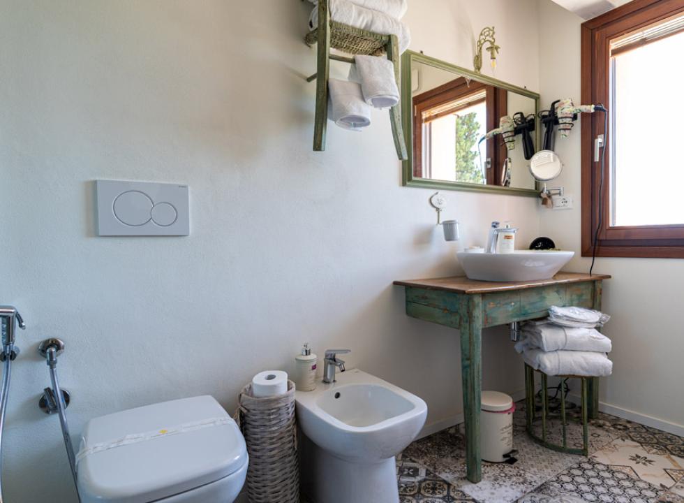 Bagno con lavabo, specchio, finestra e wc, arredato in stile rustico.